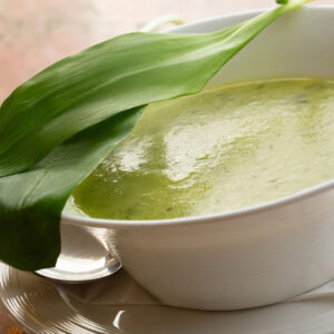 Grüne Bärlauchcremesuppe in weißer Suppenschale, dekoriert mit einem frischen Bärlauchblatt (Serviervorschlag)