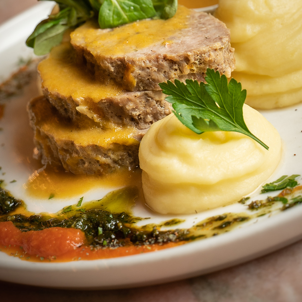 Faschierter Braten mit Erdäpfelpüree, übergossen mit Bratensaft, angerichtet mit Kräutersauce und frischer Petersilie (Serviervorschlag)