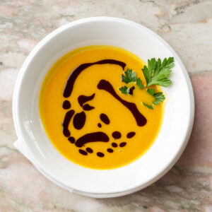 Weiße Schale mit cremiger Kürbiscremesuppe, dekoriert mit Kürbiskernöl und Petersilie (Serviervorschlag)