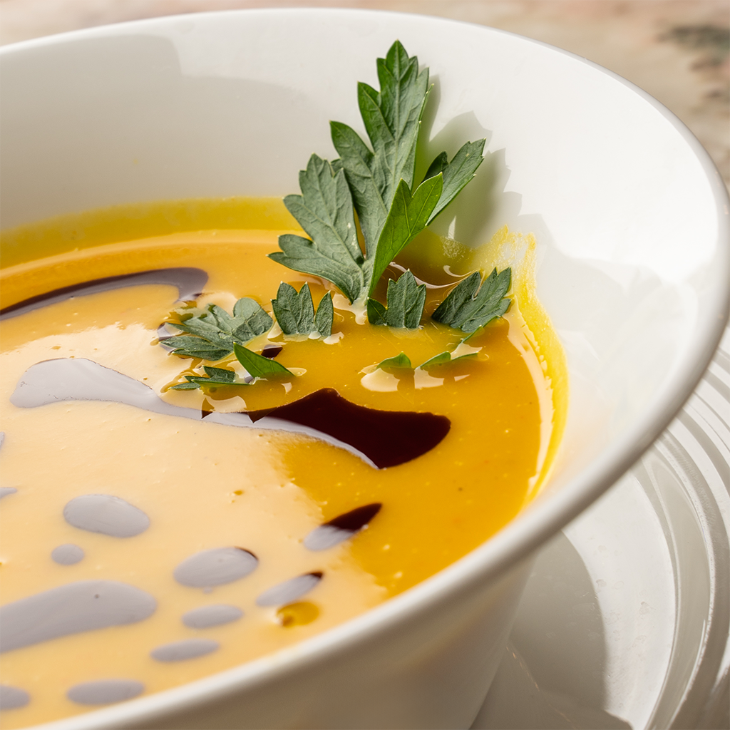 Weiße Schale mit cremiger Kürbiscremesuppe, dekoriert mit Kürbiskernöl und Petersilie (Serviervorschlag)