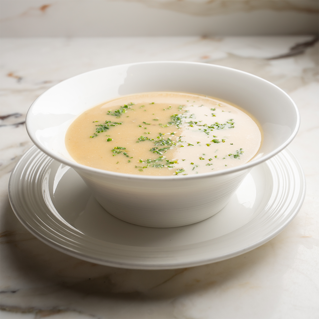 Weiße Schale mit veganer Sellerie-Birnen-Cremesuppe, fein püriert und mit Kräutern bestreut (Serviervorschlag)