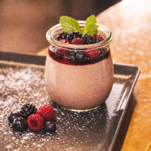 Schokoladige Grießflammerie mit Waldbeeren im Glas serviert, fein bestäubt und dekoriert (Serviervorschlag)