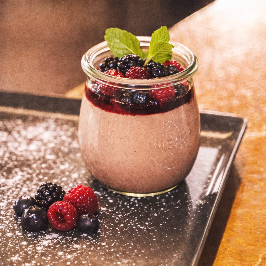 Schokoladige Grießflammerie mit Waldbeeren im Glas serviert, fein bestäubt und dekoriert (Serviervorschlag)