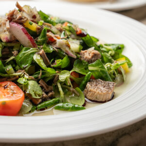 Rindfleischsalat mit Kürbiskernöl, Blattsalat und frischem Gemüse auf weißem Teller (Serviervorschlag)