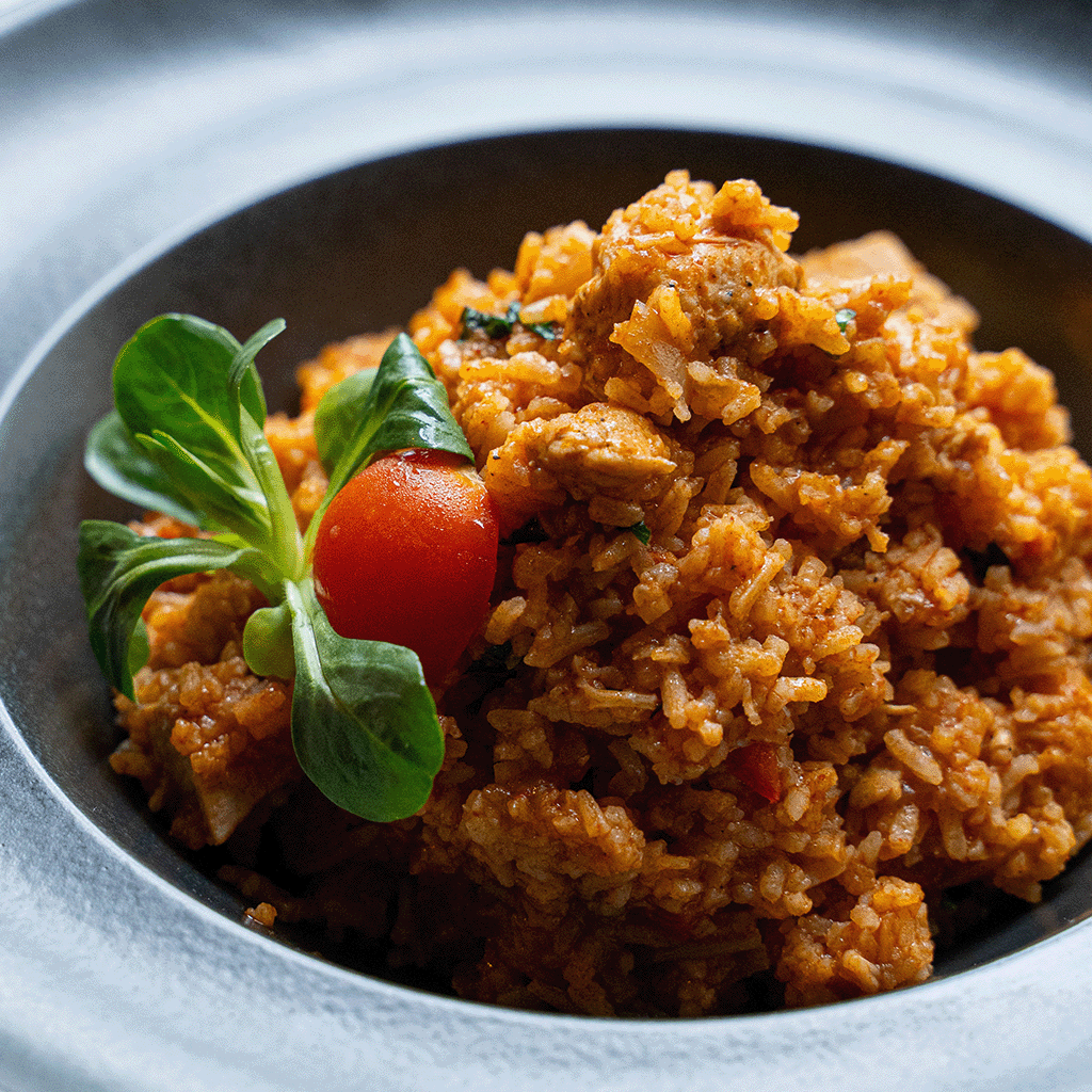 Reisfleisch mit Huhn in dunkler Schale serviert, mit saftigem Reis, zarten Hühnerstücken und Kirschtomate garniert (Serviervorschlag)