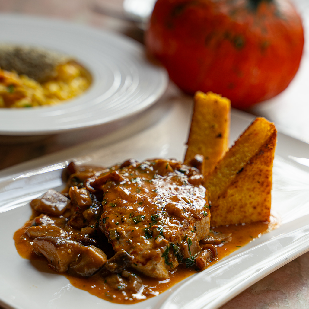 Gegrilltes Schweinskarree mit cremiger Pilzsauce und knusprig gebratener Polenta, angerichtet auf weißem Teller. (Serviervorschlag)